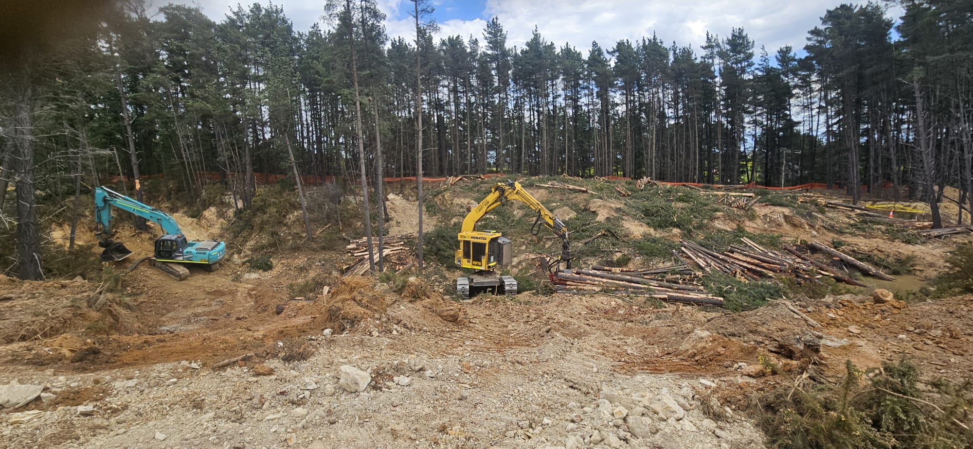 Excavator and harvester clearing vegetation for tailings dam construction