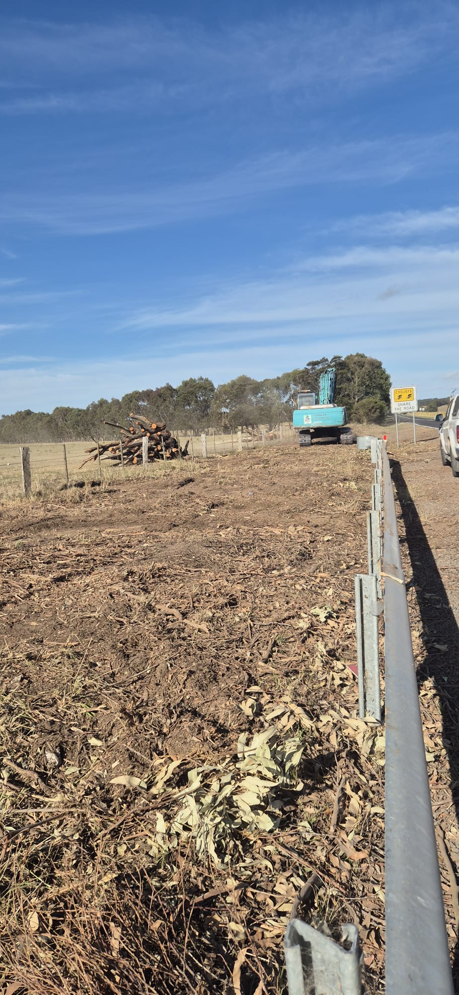 Cleared and mulched roadside verge with stockpiled timber and excavator on site